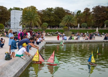 Bir baba, Fransa 'nın başkenti Paris' teki popüler Jardin du Lüksemburg 'un göletinde yelkenli yelkenli modelini denize indirirken çocuklarıyla oynar..