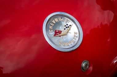 Storrington, West Sussex, İngiltere 'de klasik bir araba fuarında kırmızı bir Chevrolet Corvette' in arka bagajında çapraz bayraklı belirgin dairesel isim kartı..