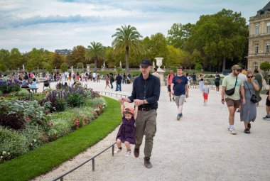 Bir baba genç kızıyla Paris, Fransa 'daki kalabalık Jardin du Lüksemburg' da yürürken oynar..