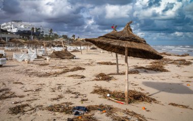 General rubbish and other detritus strewn under wind-blown parasols on Samara Beach in front of all-inclusive resorts in Sousse, Tunisia. clipart