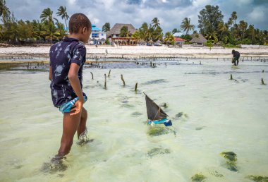 İki genç çocuk, Jambiani sahilinde, Zanzibar, Tanzanya 'da plastik sandallardan yapılan oyuncak yelkenliyle oynuyorlar.