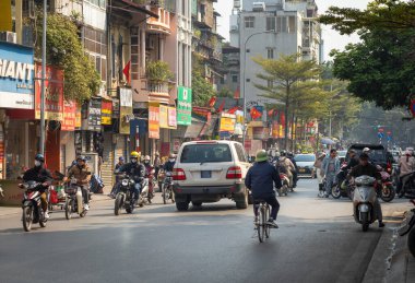 Geleneksel yeşil kollu miğfer takan Vietnamlı bir adam ağır ve kaotik trafikte Hanoi, Vietnam 'daki Kham Thien Caddesi' ndeki dükkanların önünden geçiyor.