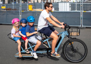 Fransa 'nın başkenti Paris' te üç küçük çocuğu sırtında taşıyan bir baba elektrikli bisiklete biniyor. Motosiklet bir Decathlon ELOPS BTWIN elektrikli arka yükleme uzun kuyruklu kargo bisikleti.