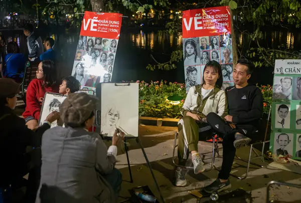 Genç bir çift, Vietnam 'ın başkenti Hanoi' de Hoan Kiem Gölü 'nün yanına portrelerini çizdirmek için oturuyor..