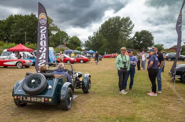 stock image Car enthusiasts watch a  participant drive his 2-seater dark green NG TD kit car (XJB 953H) from a classic car show in Storrington, West Sussex, UK.