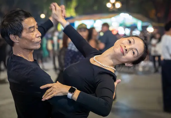 Orta yaşlı Vietnamlı bir çift geceleri sokaklarda siyah dans giyinmiş Orta Hanoi, Vietnam 'daki Hoan Kiem Gölü' nün yanında..