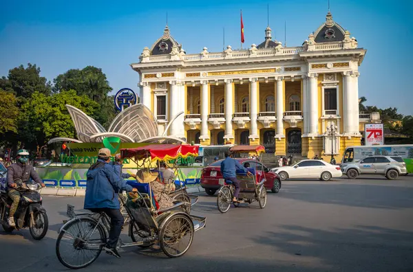 Stock image Cyclos (pedicabs) carrying tourists and other traffic passes in front of the French colonial-era Hanoi Opera House, or Nha Hat Lon, in Hanoi, Vietnam.