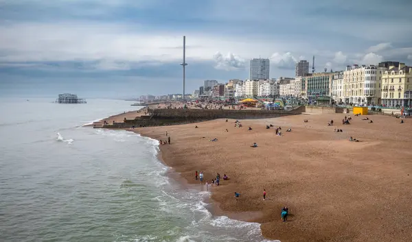 stock image A view along the beach and seafront at Brighton taken from Brighton Pier towards the ruins of the old West Pier and the i360 tower in East Sussex, UK