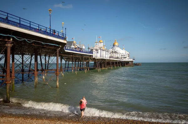 stock image A mother and daughter stand at the edge of the sea next to Eastbourne Pier in East Sussex, UK.