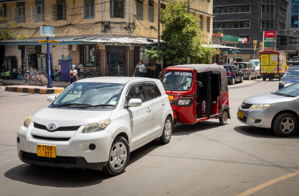 Современные автомобили и баджаджи или тук-тук, движущиеся по улице в центре Дар-эс-Салама, Танзания.