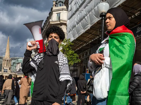 stock image London, UK. 14 Oct 2023: A masked teenage boy holds a megaphone as he stands with his mother who is wrapped in a Palestinian Flag in central London, UK, at a demonstration against Israeli attacks on Gaza.