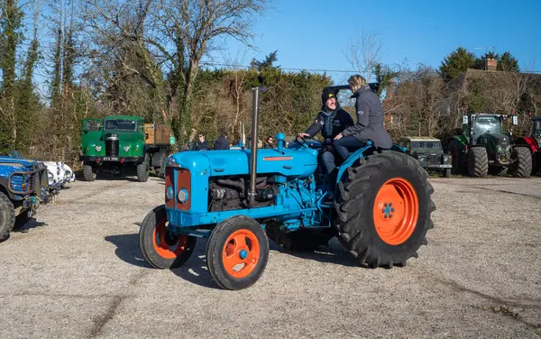 stock image A man driving a vintage Fordson tractor looks at his partner sitting on the wheel arch at a vintage tractor rally in Wisborough Green, UK.