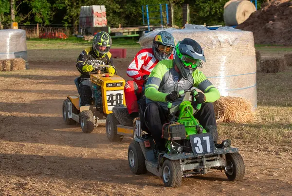 stock image Three racing lawn mower drivers jostle for position in the BLMRA 500, a Le Mans style 500 mile overnight lawn mower race in a field in West Sussex, UK.