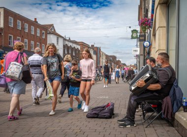 İnsanlar Newbury, Berkshire, İngiltere 'nin merkezindeki Northbrook Caddesi' nde akordeon çalan iki göçmen sokak müzisyeninin yanından geçiyor.