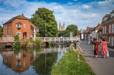 İnsanlar Kennet ve Avon Kanalı 'ndaki West Mills Swing Köprüsü' nün yanında yürürken, arka planda St Nicolas Kilisesi, Newbury, Berkshire, İngiltere.