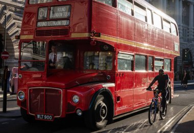 Londra turlarında kullanılan geleneksel kırmızı bir Routemaster Londra otobüsü bir bisikletçinin yanından geçer. Londra, İngiltere, İngiltere