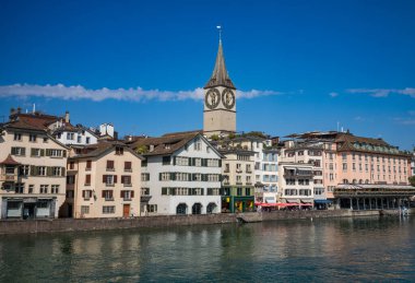 Protestan Aziz Peter Kilisesi 'nin kulesi ve büyük saati, bazıları çatı bahçeli, İsviçre' nin merkezindeki Limmat Nehri 'ni çevreleyen binalar üzerinden yükseliyor..