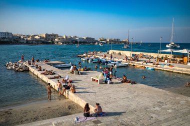 İnsanlar öğleden sonra Otranto, Apulia, İtalya 'nın merkezindeki küçük bir plaj olan Spiaggetta del Molo' da dinleniyorlar..