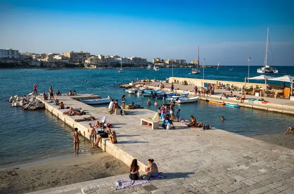 İnsanlar öğleden sonra Otranto, Apulia, İtalya 'nın merkezindeki küçük bir plaj olan Spiaggetta del Molo' da dinleniyorlar..