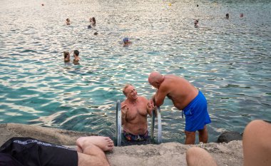 İki adam İtalyan halkının Castro Marina, Apulia, İtalya 'da dalgakıranın yanında banyo yapması ve yüzmesi hakkında konuşuyor..