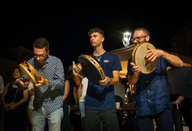İnsanlar Pizzica folk müzik grubu Canzoniere Grecanico Salentino 'nun Alessano, Lecce Eyaleti, Apulia, İtalya' da verdiği konserde tef çalıyor. Pizzica ya da Tarantula, Salento folk müziğinin bir türüdür..