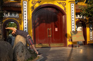 Batı Gölü, Hanoi, Vietnam 'daki antik Tran Quoc Pagoda' nın dışında sabah egzersizleri yaptığı gibi bir adam bir kayanın üzerinde geriye doğru eğilir..