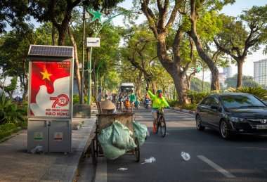 Bir kadın bisikletçi, Pazar sabahı Hanoi, Vietnam 'da Thanh Nien Yolu' ndaki bir sokak temizleyicisinin önünden geçerken el sallıyor..