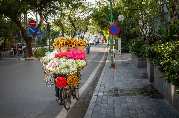Çiçekçi, nilüfer çiçekleri (Nelumbo nucifera), ortanca (Hydrangeaceae), ayçiçeği (Helianthus) ve Vietnam 'ın Hanoi kentindeki Thanh Nien Yolu' nda satılık diğer çiçekleri içeren bir bisikleti iter..