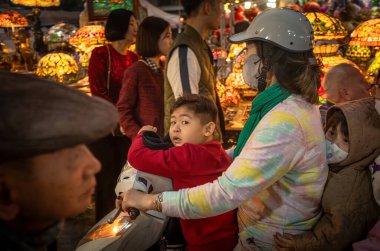 Çekici çocukları olan bir anne motosikletini kalabalık bir Tet 'ten ya da yeni yıl pazarından Hang Ma, Old Quarter, Hanoi, Vietnam' da geçirir..