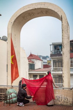 A young man helps his girlfriend pose for photographs in her traditional ao dai costume on the roof of Dong Xuan market in the Old Quarter, Hanoi, Vietnam. clipart