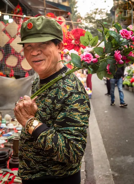 Asker tarzı zeytin yeşili giyinmiş Vietnamlı bir adam Tet 'te ya da Ay' da Hang Ruoi 'de, Vietnam' da omzunda bir demet yapay gül tutuyor..