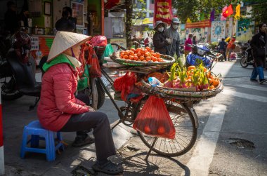 A female street vendor with a bicycle carrying flat baskets laden with fruit outside Chau Long Market, Hanoi, Vietnam. clipart