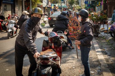 Motosikletli Vietnamlı bir çift geleneksel şeftali çiçeği dalı aldıktan sonra Chau Long pazarında, Hanoi, Vietnam.