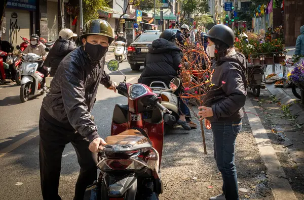 Motosikletli Vietnamlı bir çift geleneksel şeftali çiçeği dalı aldıktan sonra Chau Long pazarında, Hanoi, Vietnam.