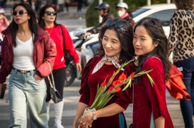Aynı kırmızı kadife elbiseli iki Vietnamlı kadın çiçek tutuyor ve fotoğraf için Tet 'e poz veriyorlar, ya da yeni yıl, Hanoi, Vietnam' da..