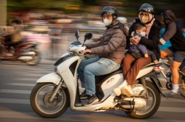 Yüz maskesi takan Vietnamlı bir karı koca küçük oğullarını orta Hanoi, Vietnam 'da aile motosikletinde taşıyorlar..