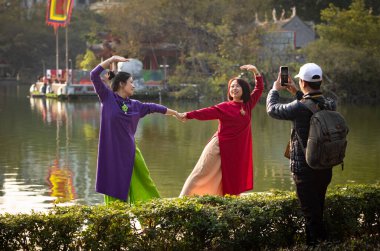 Geleneksel ao dai gibi giyinmiş iki Vietnamlı kadın el ele tutuşmuş ve Hoan Kiem Gölü, Hanoi, Vietnam 'da poz vermek için kalp şeklinde şekillenmişler.