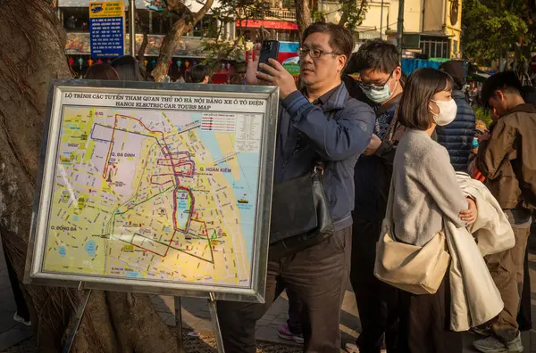 Asyalı turistler Dinh Tien Hoang, Hanoi, Vietnam 'daki Hanoi Elektrikli Otomobil Turlarının güzergahlarını gösteren haritanın yanında bekliyorlar.