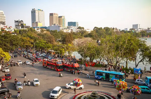 Açık turistik otobüslere, arabalara, motosikletlere ve Hoan Kiem Gölü 'nün kuzey ucundaki insanlara bakıyorum..