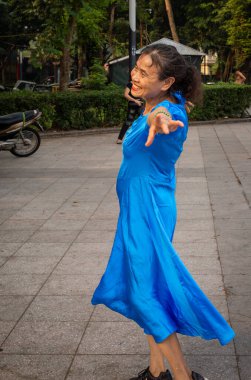 Mavi elbiseli emekli bir kadın sabah egzersizi için Lenin Park, Hanoi, Vietna 'da dans ediyor.,.