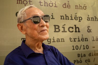 Güneş gözlüğü takan yaşlı Vietnamlı bir adam Hanoi, Vietnam 'da bir fotoğraf sergisini ziyaret ediyor.