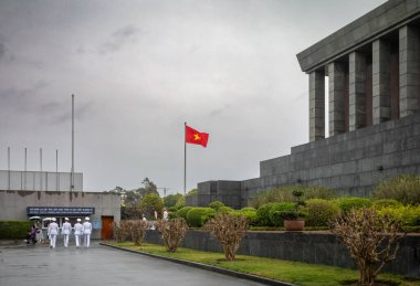 Ho Chi Minh Anıt Mezar Komutanlığı Onur Muhafızları 'ndan beyaz üniformalı askerler mozolenin ve Vietnam bayrağının yanında yürüyorlar.
