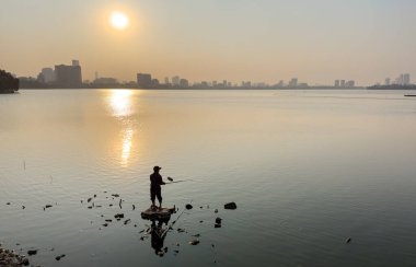 Bir adam akşamüstü Batı Gölü, Hanoi, Vietnam 'da terk edilmiş bir teknenin yanında balık tutuyor..
