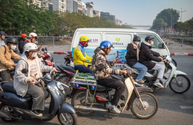 Motosiklet kullanan bir adam, Lich Nehri 'nin üzerindeki Cau Giay, Hanoi, Vietnam' daki bir köprüde motosiklet trafiğinin arasında cep telefonuna bakıyor.