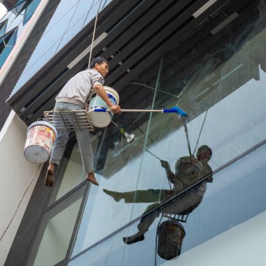 Bir adam, Dong Da, Hanoi, Vietnam 'da cam kaplı modern bir ofis binasının camlarını silerken iple sallanıyor..