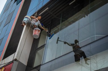 Bir adam, Dong Da, Hanoi, Vietnam 'da cam kaplı modern bir ofis binasının camlarını silerken iple sallanıyor..