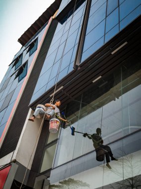 Bir adam, Dong Da, Hanoi, Vietnam 'da cam kaplı modern bir ofis binasının camlarını silerken iple sallanıyor..