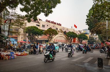 Motosikletler, arabalar ve insanlar Hanoi, Vietnam 'daki ünlü Dong Xuan pazarının önünde koşuşturuyorlar.