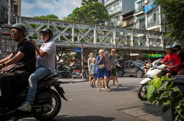 Yetişkin ve çocuklardan oluşan bir grup Batılı turist Hanoi, Vietnam 'ın merkezinde yoğun bir yoldan geçiyor..