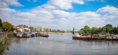 Viktorya dönemi Hammersmith Köprüsü yakınlarındaki Thames nehrine demirlemiş dönüştürülmüş mavnalar ve yüzen evlerden oluşan bir panorama..
